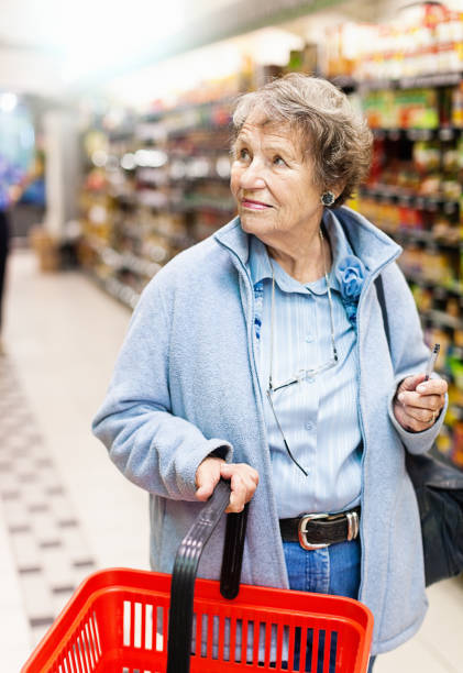 donna anziana con carrello della spesa al supermercato - senior adult aging process supermarket shopping foto e immagini stock
