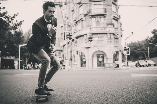 Handsome modern man standing on the street in big city, riding skateboard, black and white.