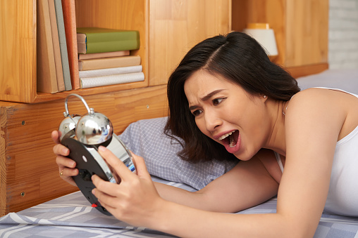 Overslept young Asian woman looking at her alarm clock