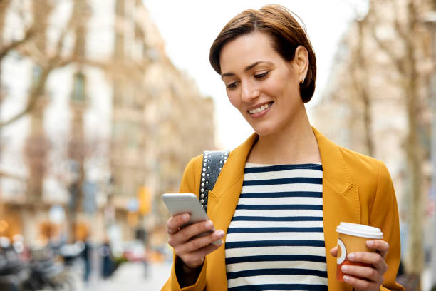 istock Smiling woman with disposable cup texting in city 948887940