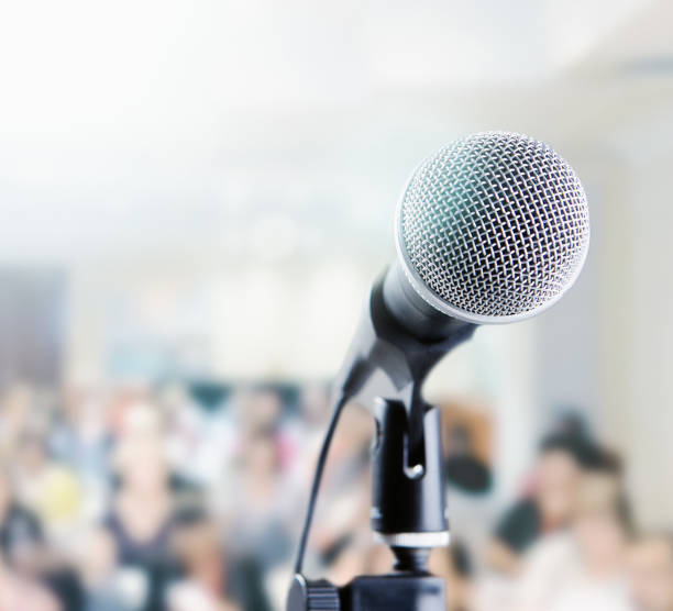 istock Microphone waits in front of brightly lit, defocused audience 948895024