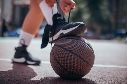 Girl tying shoelace before streetball game outdoors, foot on the basketball ball.