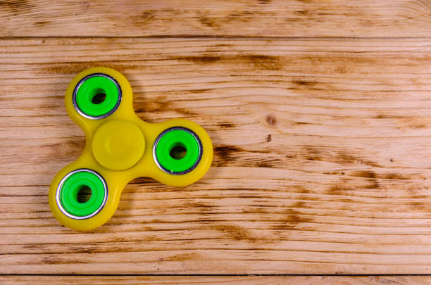 istock Yellow fidget spinner on wooden desk. Top view 948905892