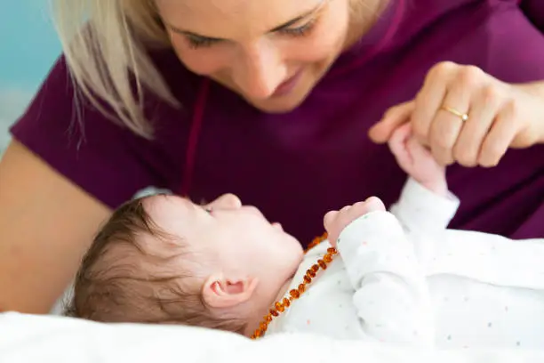 beautiful blond mother with her 3 month old baby wearing a amber necklace lying in bed