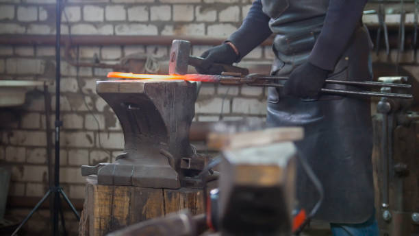 istock Muscular man blacksmith with hammer in forge creating steel knife 948920516