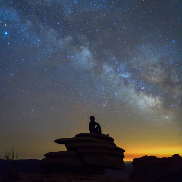 istock Man sitting on the rock under The Milky Way Galaxy 948921674