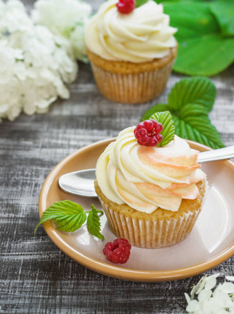 istock Delicate vanilla cupcakes with cream and raspberries on a dark wooden background 948932826