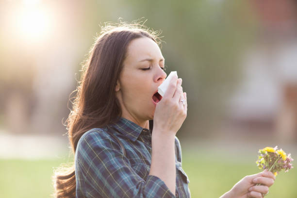 Woman sneezing in park with flowers in other hand Young pretty woman sneezing and blowing nose while holding bouquet of spring flowers from meadow. Pollen allergy symptoms sinusitis photos stock pictures, royalty-free photos & images
