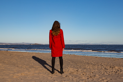 One young woman in a red coat looking out to sea.