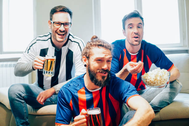 istock Male football supporters making funny faces and having a snack while watching the game 949032094