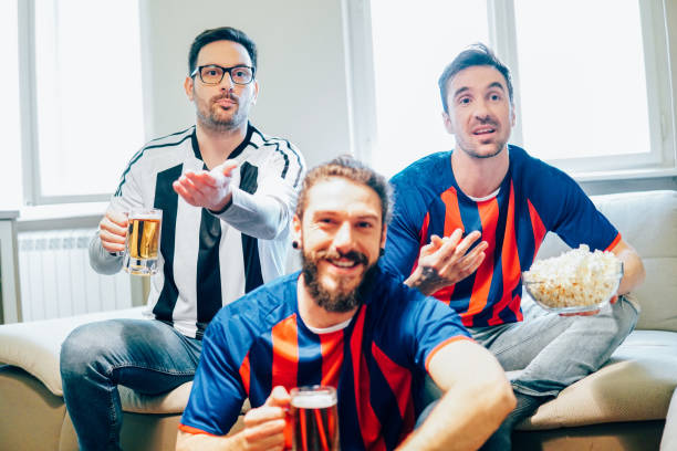 istock Men drinking beer and eating popcorn watching soccer game together 949032100