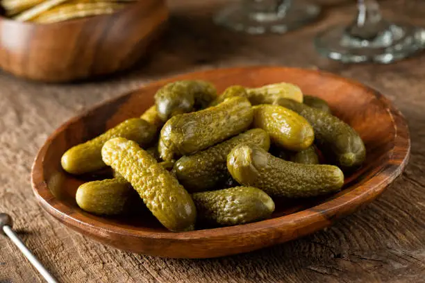 A bowl of baby dill pickles on a rustic wood table top.