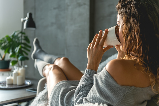 Beautiful young woman holding cup of coffee, holding legs on the table