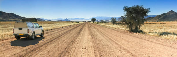 ピックアップ トラックが山に向かってまっすぐ長い砂漠の道路で運転。 - landscape panoramic kalahari desert namibia ストックフォトと画像