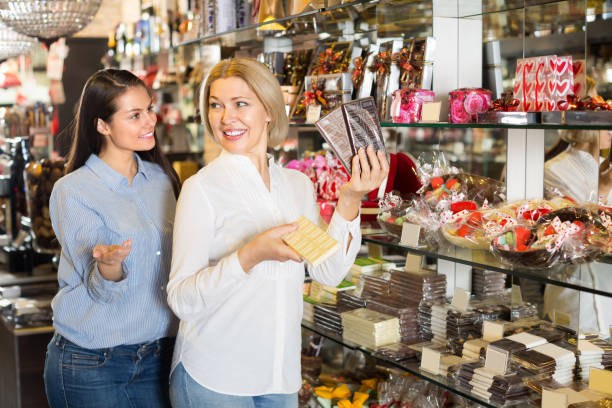 Happy women buying chocolate bars Two happy women choosing dark and white chocolate bars at store and smiling. Selective focus old candy store stock pictures, royalty-free photos & images