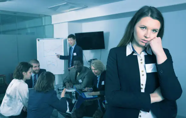Portrait of unhappy adult woman in boardroom on background with working business colleagues