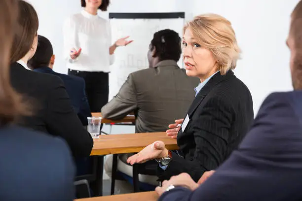 Surprised pleasant mature business woman talking with people during conference in meeting room