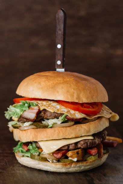 istock Big hamburger pinned with knife on wood background 949107114