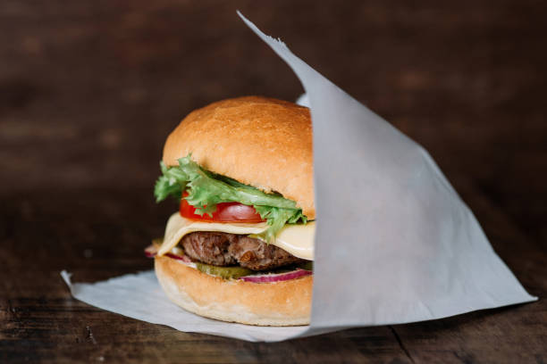 istock fresh tasty burger wrapped on white paper on wooden table. With empty place for title 949107380