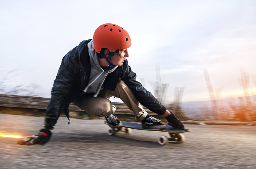 Young man in helmet is going to slide, slide with sparks on a longboard on the asphalt at sunset