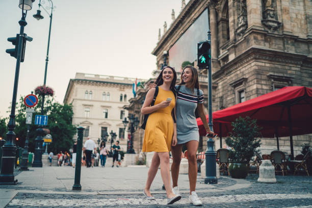 Young women in Budapest crossing the street at the pedestrian walkway Happy friends in the city crossing the street and smiling crossing sign stock pictures, royalty-free photos & images