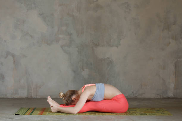 istock Young woman practicing left seated forward bend / Paschimottanasana yoga pose against texturized wall / urban background 949126938