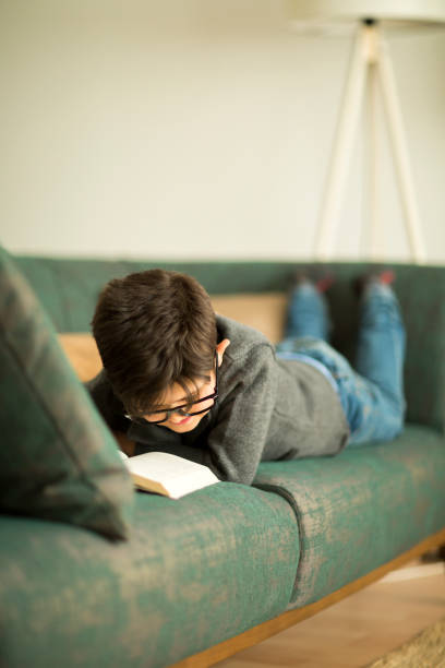 istock Little boy reading a book in armchair 949127818