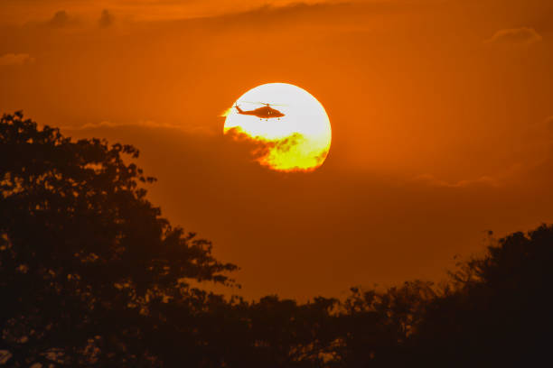 The helicopter is flying through the sun in the evening.