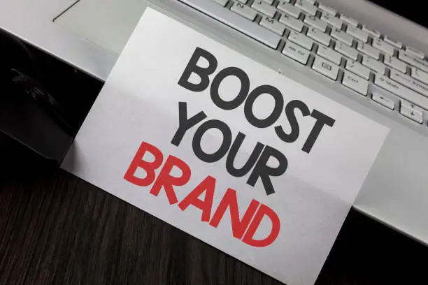 Photo of Writing note showing  Boost Your Brand. Business photo showcasing improve your models name in your field overcome competitors written on White Sticky Note Paper placed on wooden Table Laptop Mouse