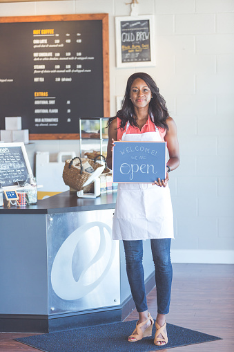 Attractive African American coffeehouse owner holds up a sign that reads 