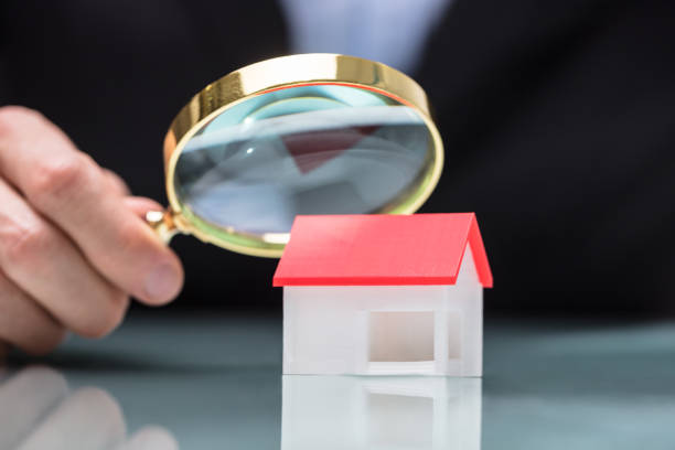 istock Businessperson Looking At House Model Through Magnifying Glass 949178114