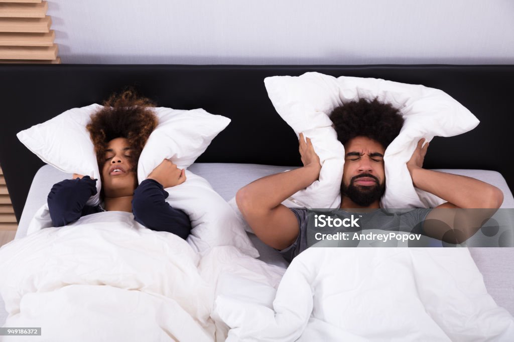 Young Couple Covering Their Ears With Pillow Elevated View Of Young Couple Lying In Bed Covering Their Ears With Pillow Noise Stock Photo