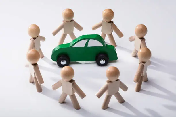 Green Car Surrounded By Wooden Human Figures On White Background