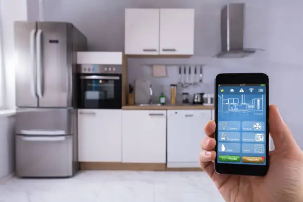 Close-up Of A Person's Hand Using Smart Home System On Mobilephone In Kitchen