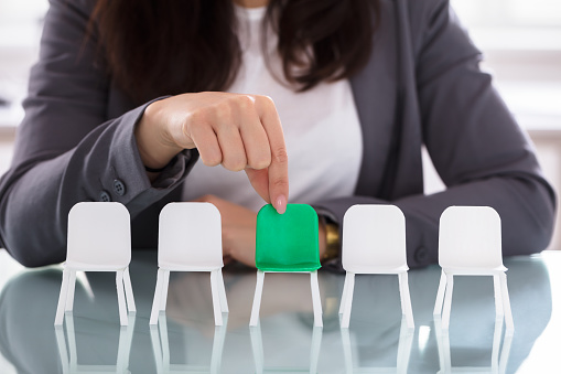 Close-up Of A Businesswoman's Hand Choosing Green Chair Among White Chairs In A Row