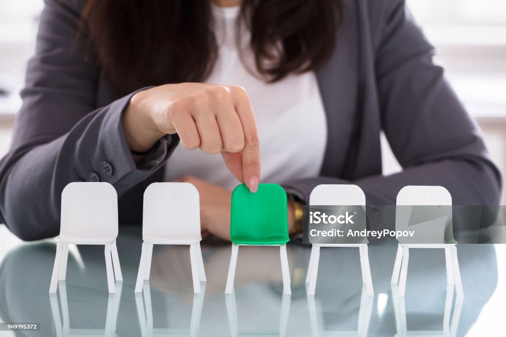 Businesswoman Choosing Green Chair Among White Chairs In A Row Close-up Of A Businesswoman's Hand Choosing Green Chair Among White Chairs In A Row Job Interview Stock Photo