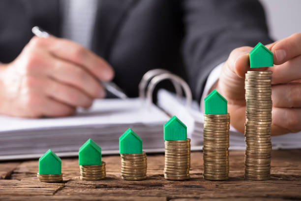 istock Businessperson Placing House Model On Increasing Stacked Coins 949199138