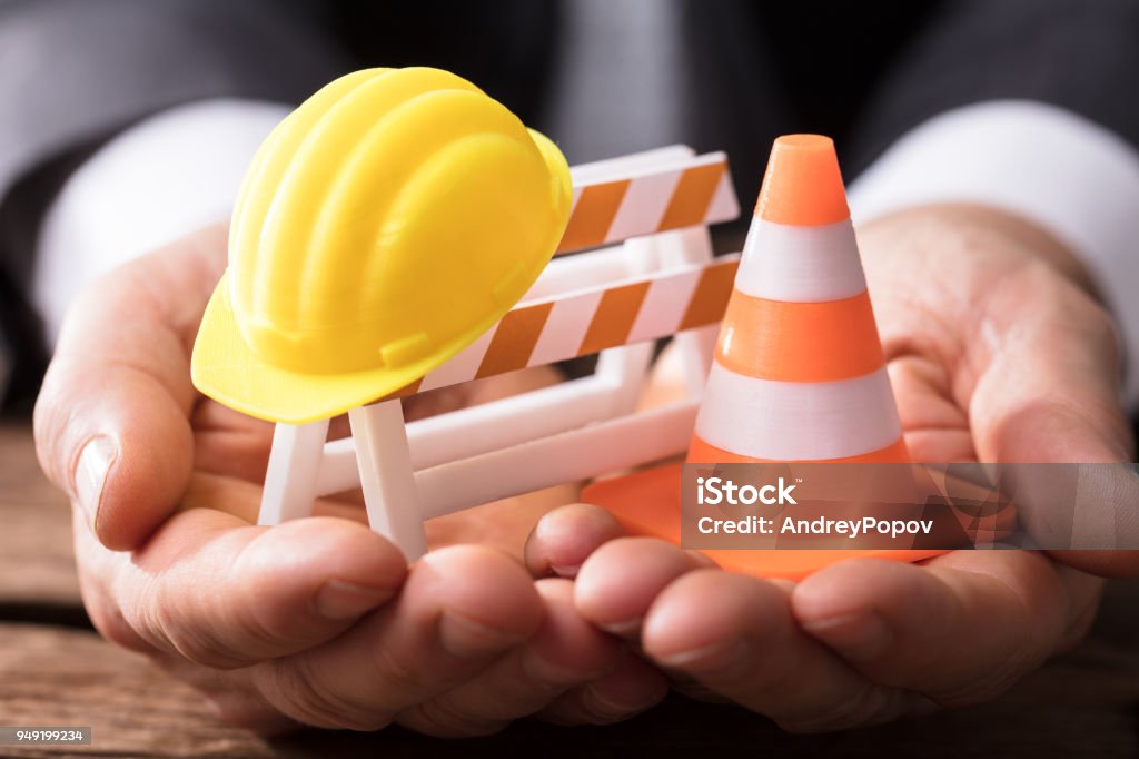 Close-up Of Barricade With Traffic Cone And Hard Hat Close-up Of Human Hand Holding Barricade With Traffic Cone And Hard Hat Occupational Safety And Health Stock Photo