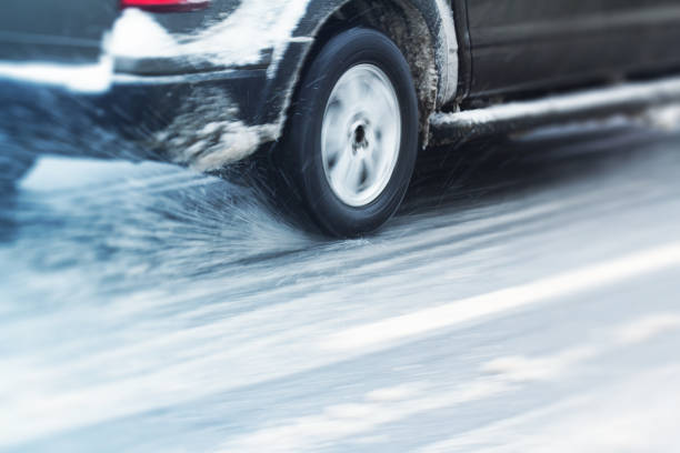 closeup rear view of a car dark color wheel tire going through snow on a city road traffic with motion blur