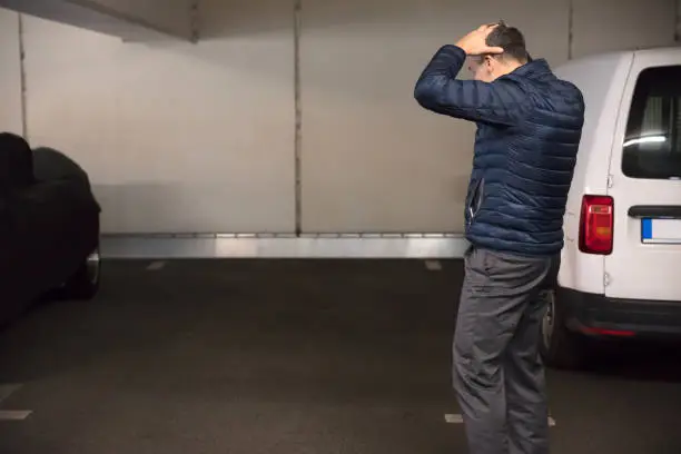 Rear View Of A Shocked Man Standing In Parking Lot After His Car Was Stolen