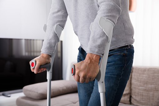 Mid Section View Of A Man With Broken Leg Using Crutches At Home