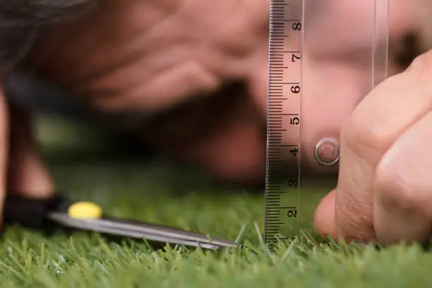 Photo of Man Using Measuring Scale While Cutting Grass