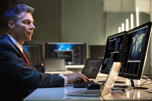 Side View Of A Mature Businessman Working On Multiple Computers In Office