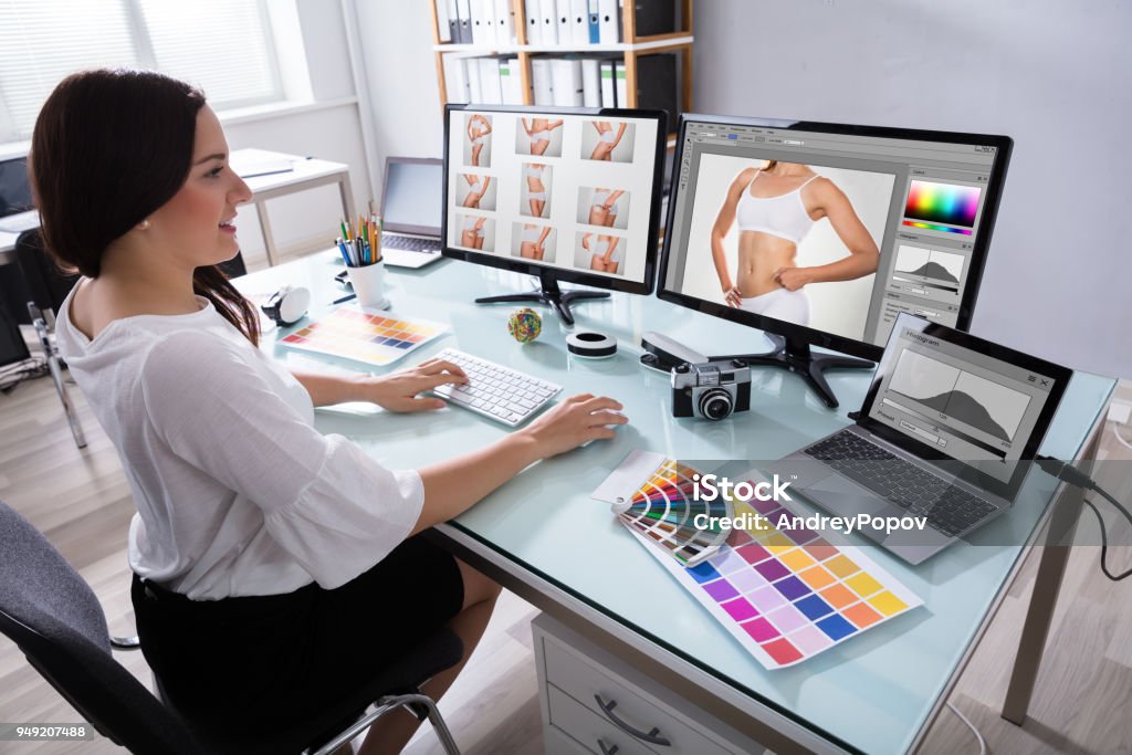 Female Designer Working With Photographs On Multiple Computer Happy Young Female Designer Working With Photographs On Multiple Computer At Workplace Retouched Image Stock Photo
