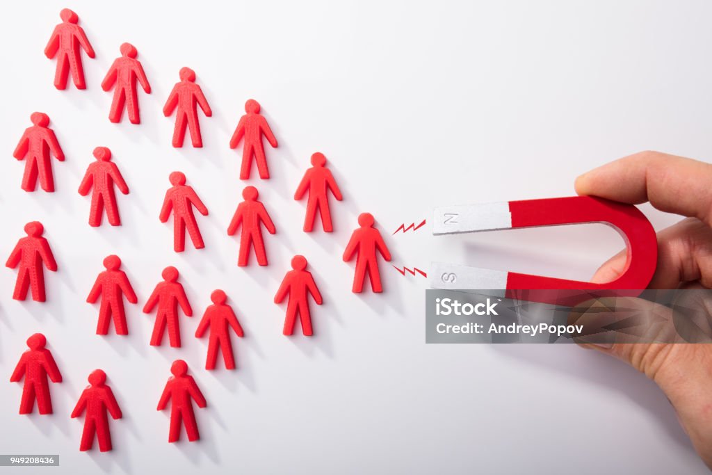 Human Hand Attracting Human Figures With Horseshoe Magnet Close-up Of A Human Hand Attracting Red Human Figures With Horseshoe Magnet On White Background Lead Stock Photo
