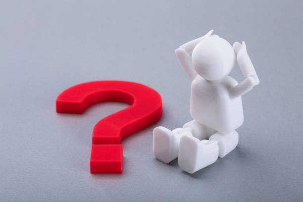 Close-up Of A Human Figure Sitting Beside Red Question Mark Sign On Grey Background