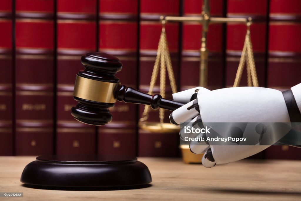 Robot Striking Gavel On Sounding Block Close-up Of A Robotic Hand Striking Gavel On Sounding Block In Courtroom Artificial Intelligence Stock Photo