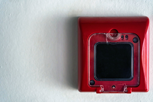 Closeup of red fire alarm box with black button on white wall background