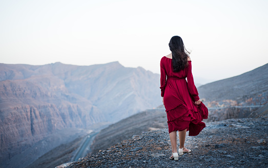 Fashionable girl on a desert mountain top wearing red dress