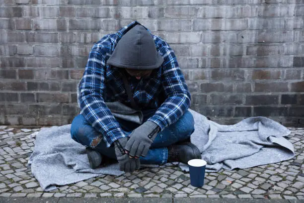 Side View Of A Male Beggar Sitting On Street Near Disposable Cup